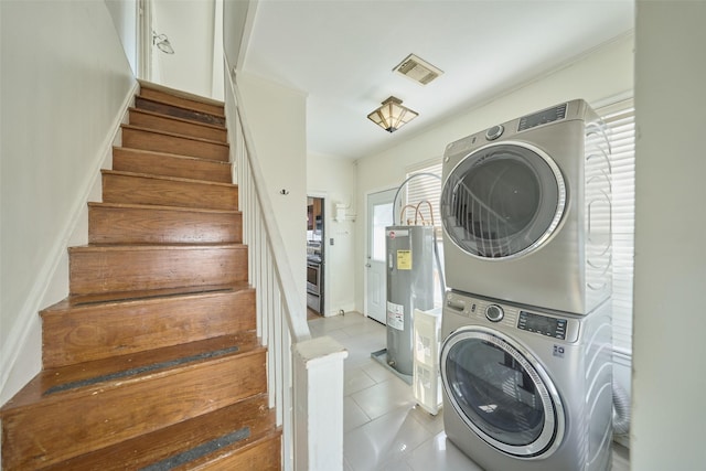 laundry room featuring visible vents, water heater, laundry area, stacked washing maching and dryer, and tile patterned floors