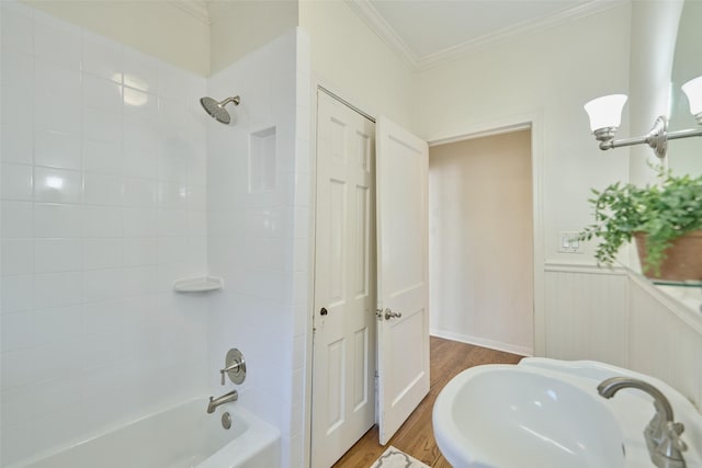 bathroom with a wainscoted wall, ornamental molding, a sink, wood finished floors, and bathing tub / shower combination