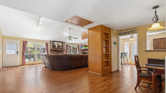 living area with track lighting, built in features, wood finished floors, and ceiling fan