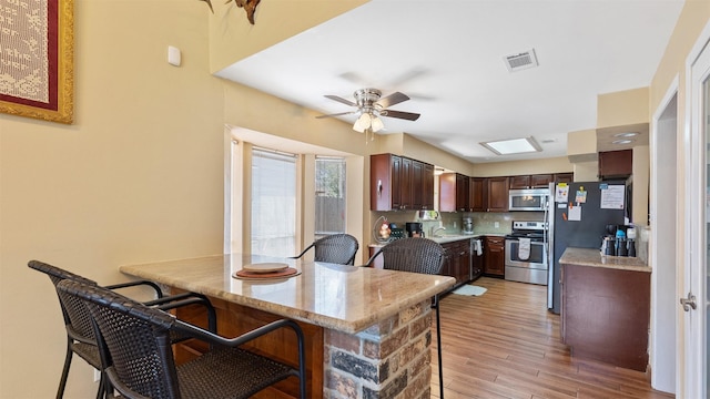 kitchen featuring visible vents, decorative backsplash, a kitchen breakfast bar, stainless steel appliances, and a ceiling fan