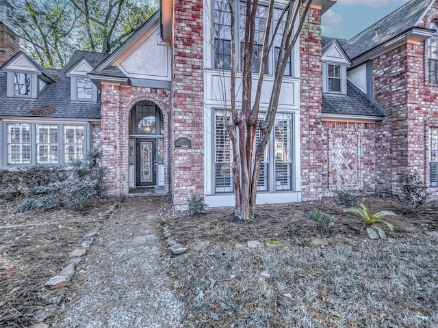 entrance to property with brick siding, roof with shingles, and a chimney