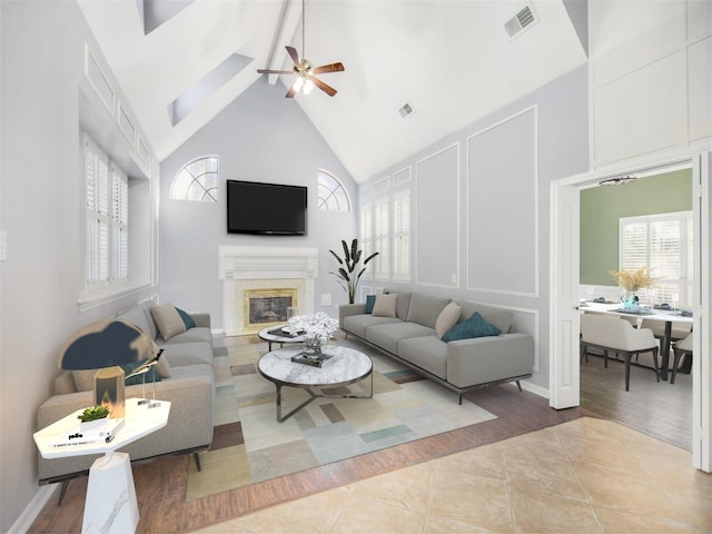 tiled living room with visible vents, high vaulted ceiling, a ceiling fan, a fireplace, and a decorative wall