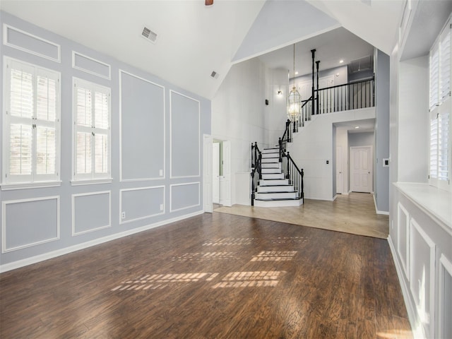 entryway with visible vents, high vaulted ceiling, wood finished floors, a decorative wall, and stairs