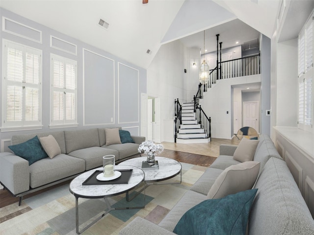 living room featuring visible vents, high vaulted ceiling, wood finished floors, stairway, and a decorative wall