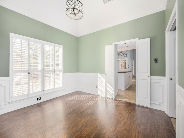 unfurnished room with a wainscoted wall, an inviting chandelier, and wood finished floors