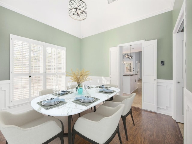 dining area featuring a notable chandelier, dark wood finished floors, wainscoting, a decorative wall, and crown molding