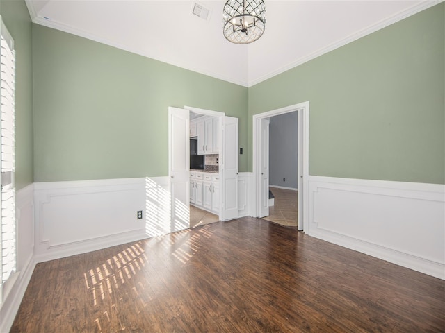 unfurnished room featuring a notable chandelier, visible vents, a wainscoted wall, and wood finished floors