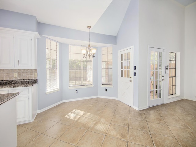 unfurnished dining area featuring baseboards, high vaulted ceiling, an inviting chandelier, and light tile patterned flooring