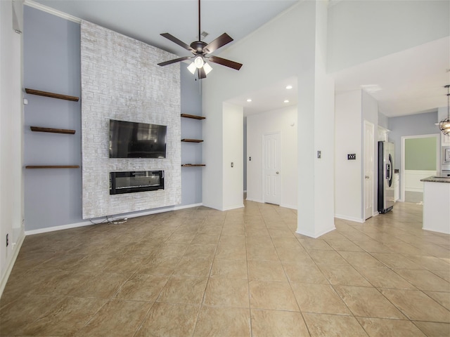 unfurnished living room with light tile patterned floors, a towering ceiling, ceiling fan, and a fireplace