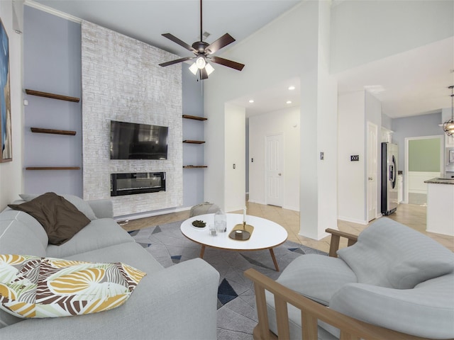 living room with light tile patterned floors, a high ceiling, a stone fireplace, and a ceiling fan