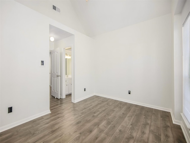 empty room featuring visible vents, baseboards, wood finished floors, and vaulted ceiling