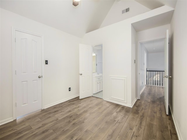 unfurnished bedroom featuring visible vents, baseboards, attic access, vaulted ceiling, and wood finished floors