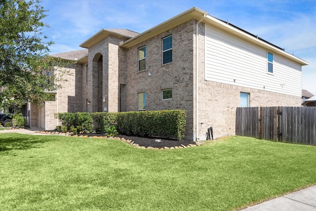 view of side of home with brick siding, a lawn, and fence