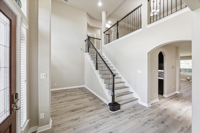 foyer featuring a high ceiling, wood finished floors, arched walkways, and baseboards