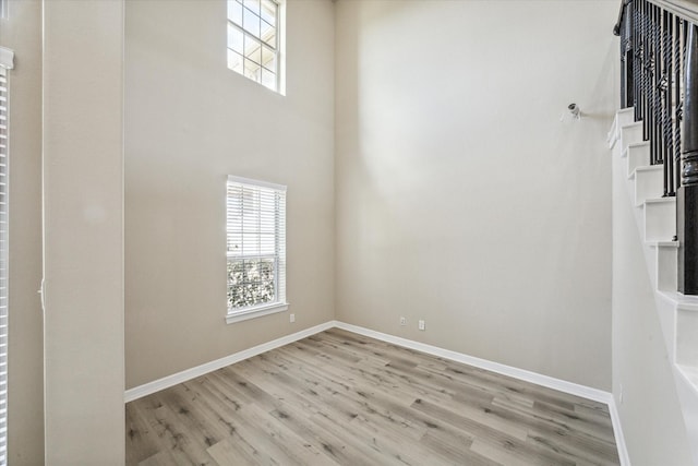 spare room featuring wood finished floors, baseboards, and a towering ceiling