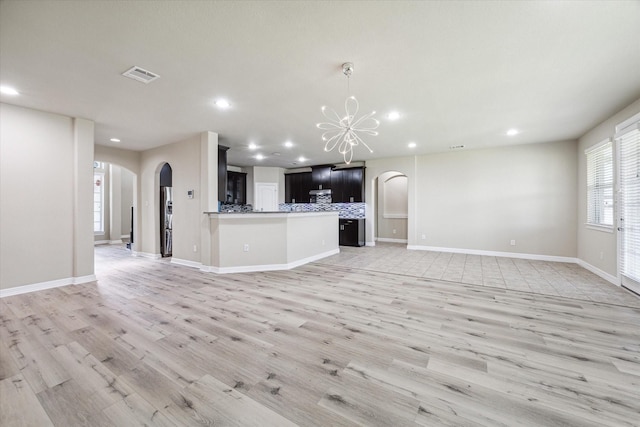 unfurnished living room featuring light wood-type flooring, visible vents, arched walkways, and an inviting chandelier