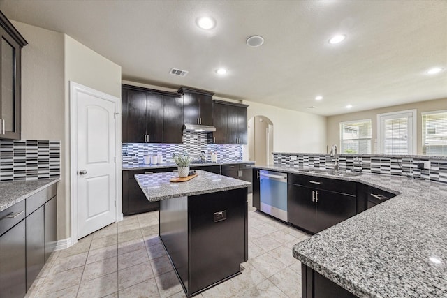 kitchen with visible vents, a kitchen island, arched walkways, a sink, and stainless steel dishwasher