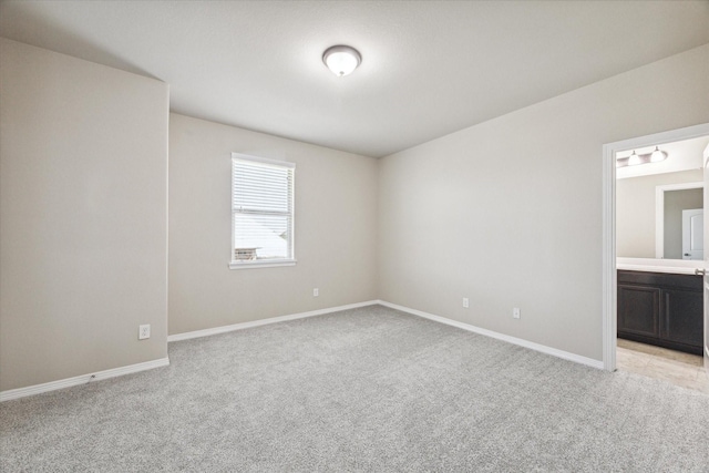 unfurnished bedroom with ensuite bath, light colored carpet, and baseboards