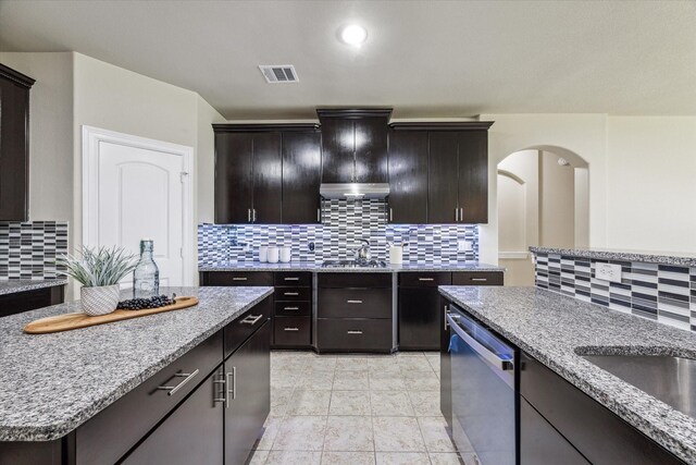 kitchen with light stone countertops, visible vents, decorative backsplash, under cabinet range hood, and dishwasher