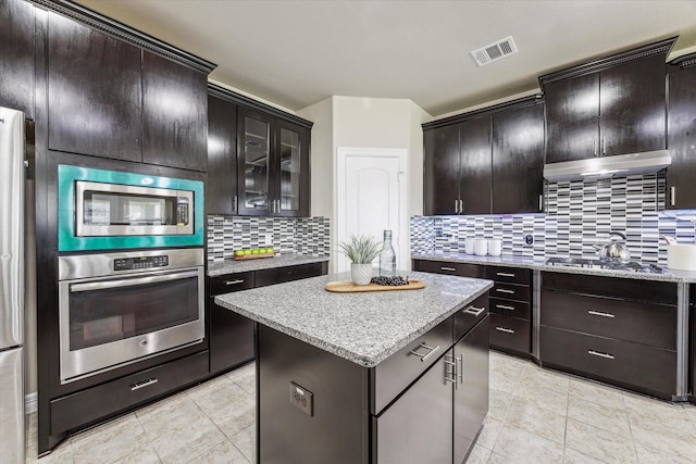 kitchen with tasteful backsplash, visible vents, a center island, under cabinet range hood, and appliances with stainless steel finishes