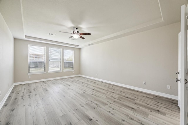 empty room with visible vents, baseboards, light wood finished floors, a raised ceiling, and ceiling fan