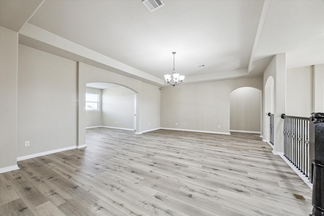 unfurnished room featuring a notable chandelier, arched walkways, a raised ceiling, and visible vents