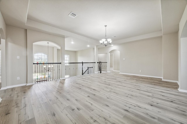 unfurnished room with visible vents, wood finished floors, arched walkways, an inviting chandelier, and baseboards