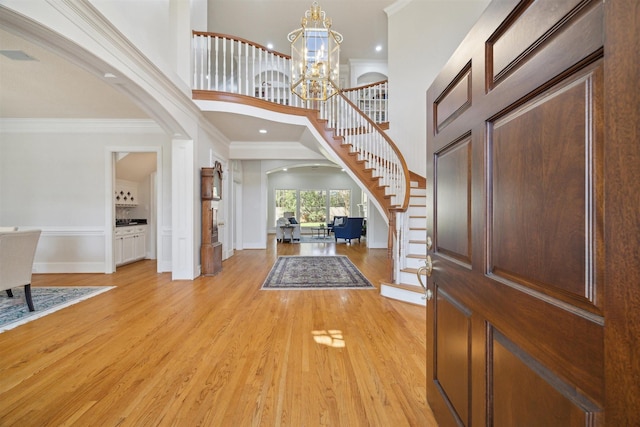 entryway with an inviting chandelier, light wood-style floors, arched walkways, and ornamental molding