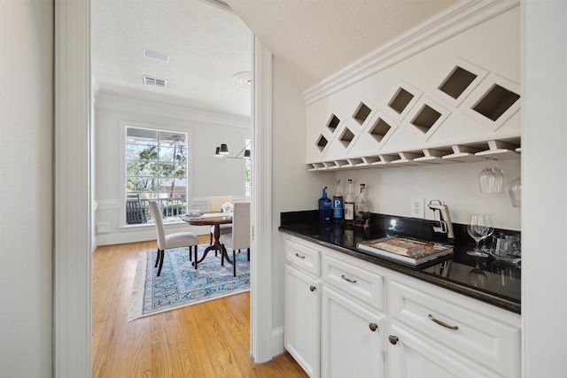 bar with visible vents, crown molding, light wood-style floors, and indoor bar