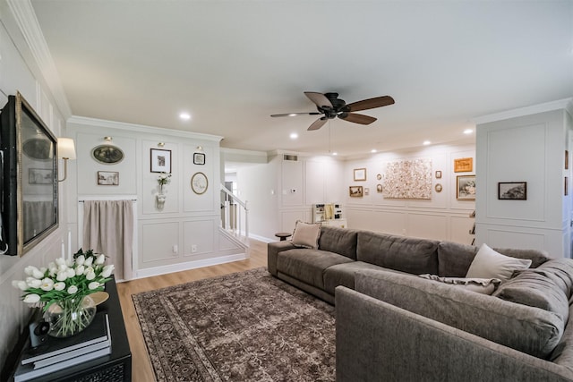 living room with stairway, light wood-type flooring, a ceiling fan, and ornamental molding