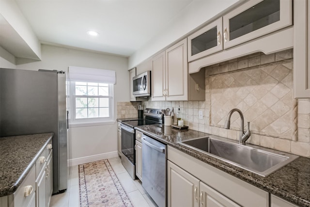 kitchen with baseboards, a sink, stainless steel appliances, glass insert cabinets, and tasteful backsplash