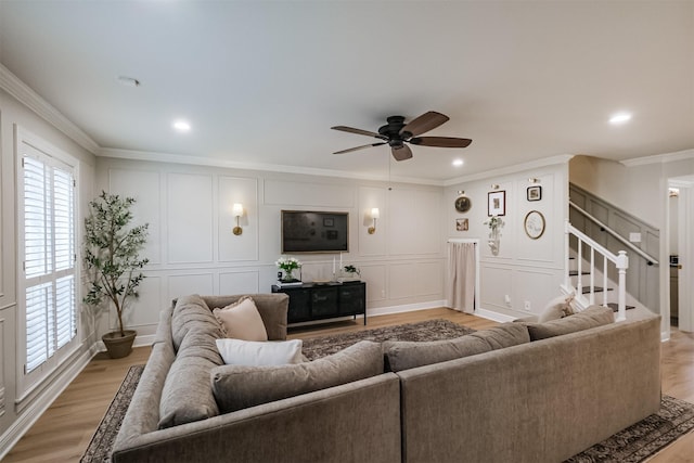 living area featuring light wood-style floors, ceiling fan, ornamental molding, and a decorative wall