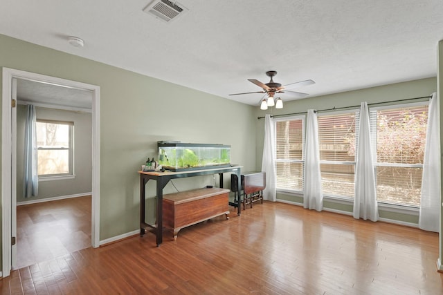 living area featuring visible vents, baseboards, ceiling fan, and hardwood / wood-style floors