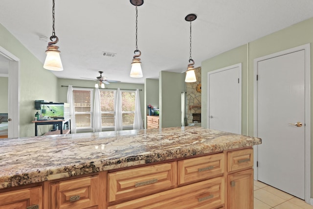 kitchen with light stone counters, light tile patterned floors, visible vents, ceiling fan, and decorative light fixtures