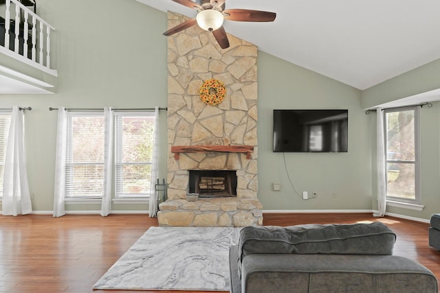 living area featuring ceiling fan, a healthy amount of sunlight, wood finished floors, and a stone fireplace