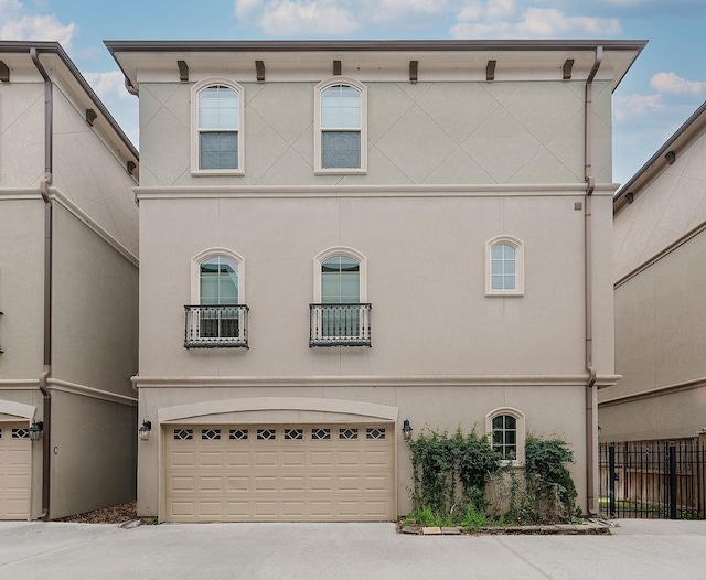 view of front facade featuring a balcony, stucco siding, a garage, and fence