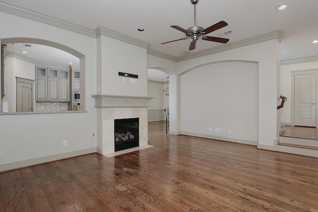 unfurnished living room with visible vents, ornamental molding, wood finished floors, arched walkways, and ceiling fan