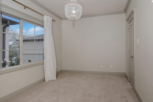 carpeted spare room featuring a notable chandelier, baseboards, and ornamental molding