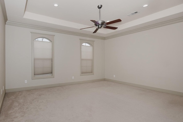 empty room with a ceiling fan, visible vents, a tray ceiling, light carpet, and crown molding