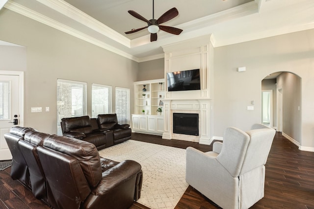 living room featuring a ceiling fan, a tray ceiling, arched walkways, dark wood-style flooring, and crown molding