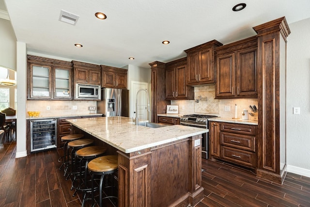 kitchen featuring visible vents, wood finish floors, a sink, stainless steel appliances, and wine cooler