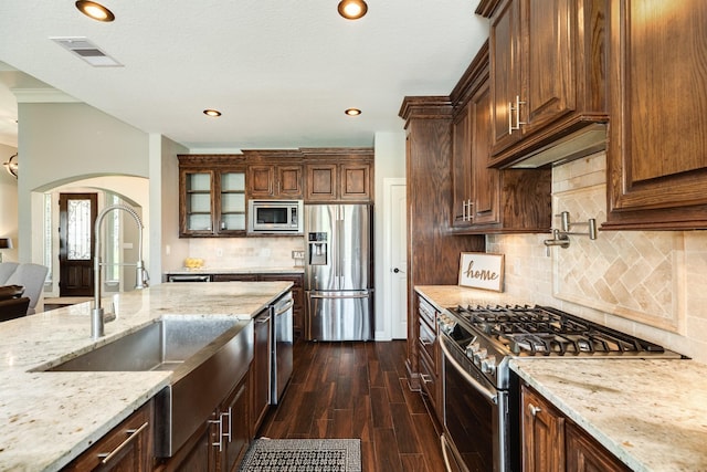 kitchen featuring light stone counters, visible vents, arched walkways, a sink, and appliances with stainless steel finishes