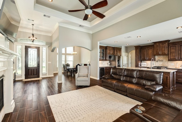 living room featuring a ceiling fan, dark wood-style floors, wine cooler, arched walkways, and a raised ceiling