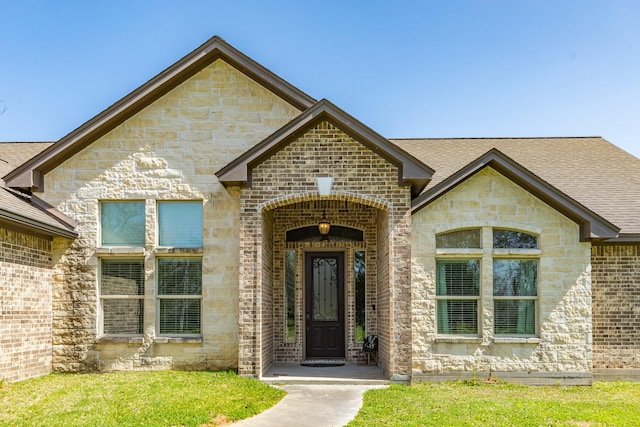 view of exterior entry featuring brick siding, stone siding, and roof with shingles