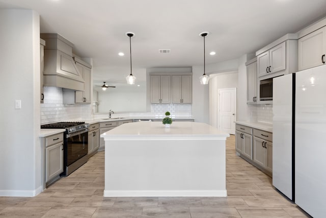 kitchen with gray cabinetry, a kitchen island, light countertops, gas range, and ceiling fan