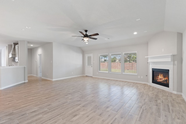 unfurnished living room featuring a glass covered fireplace, light wood-style flooring, a ceiling fan, and baseboards