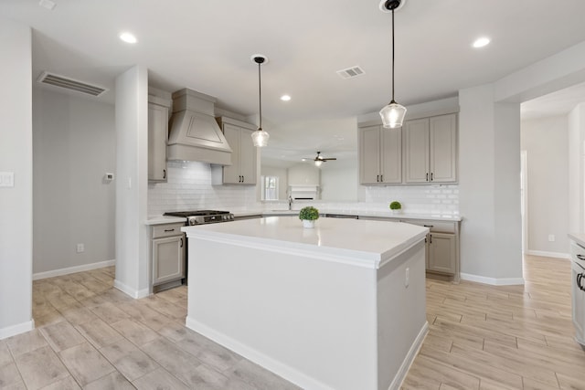 kitchen featuring visible vents, custom range hood, a sink, a kitchen island, and light countertops