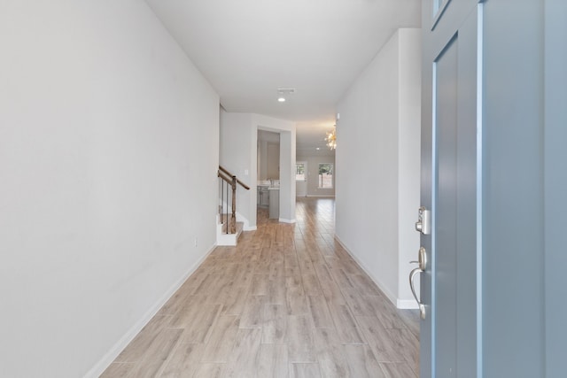 hallway with baseboards, stairs, and light wood-style floors