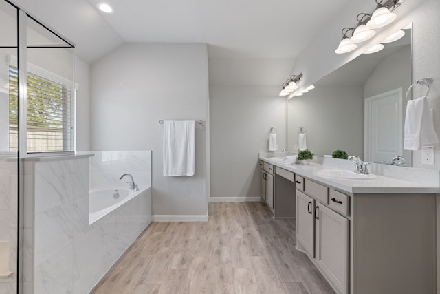 bathroom with a garden tub, a sink, wood finished floors, double vanity, and vaulted ceiling