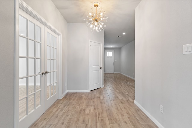 corridor featuring an inviting chandelier, light wood-style floors, baseboards, and visible vents